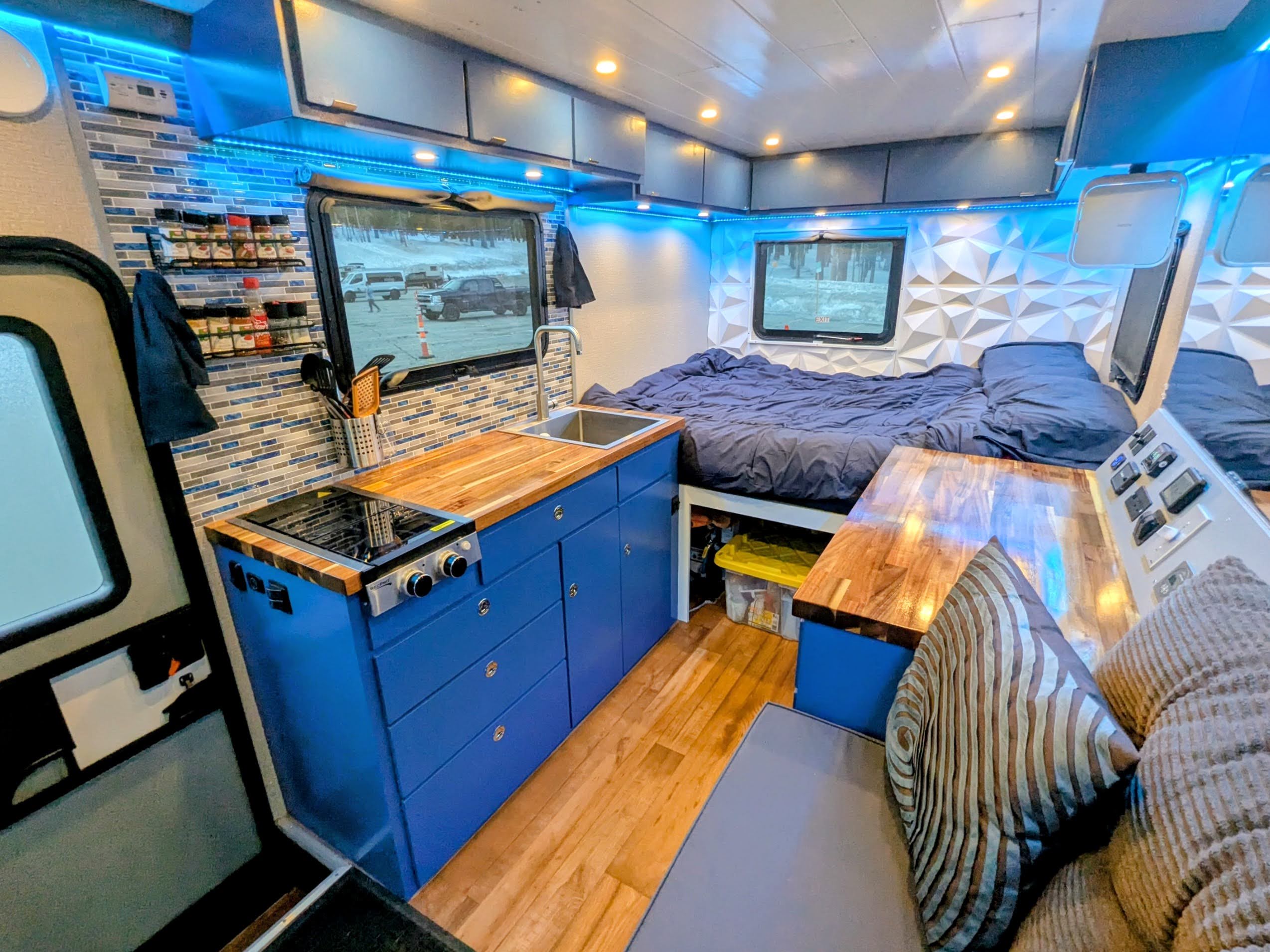 Custom campervan kitchen with butcher block counters, blue cabinetry, and full bed